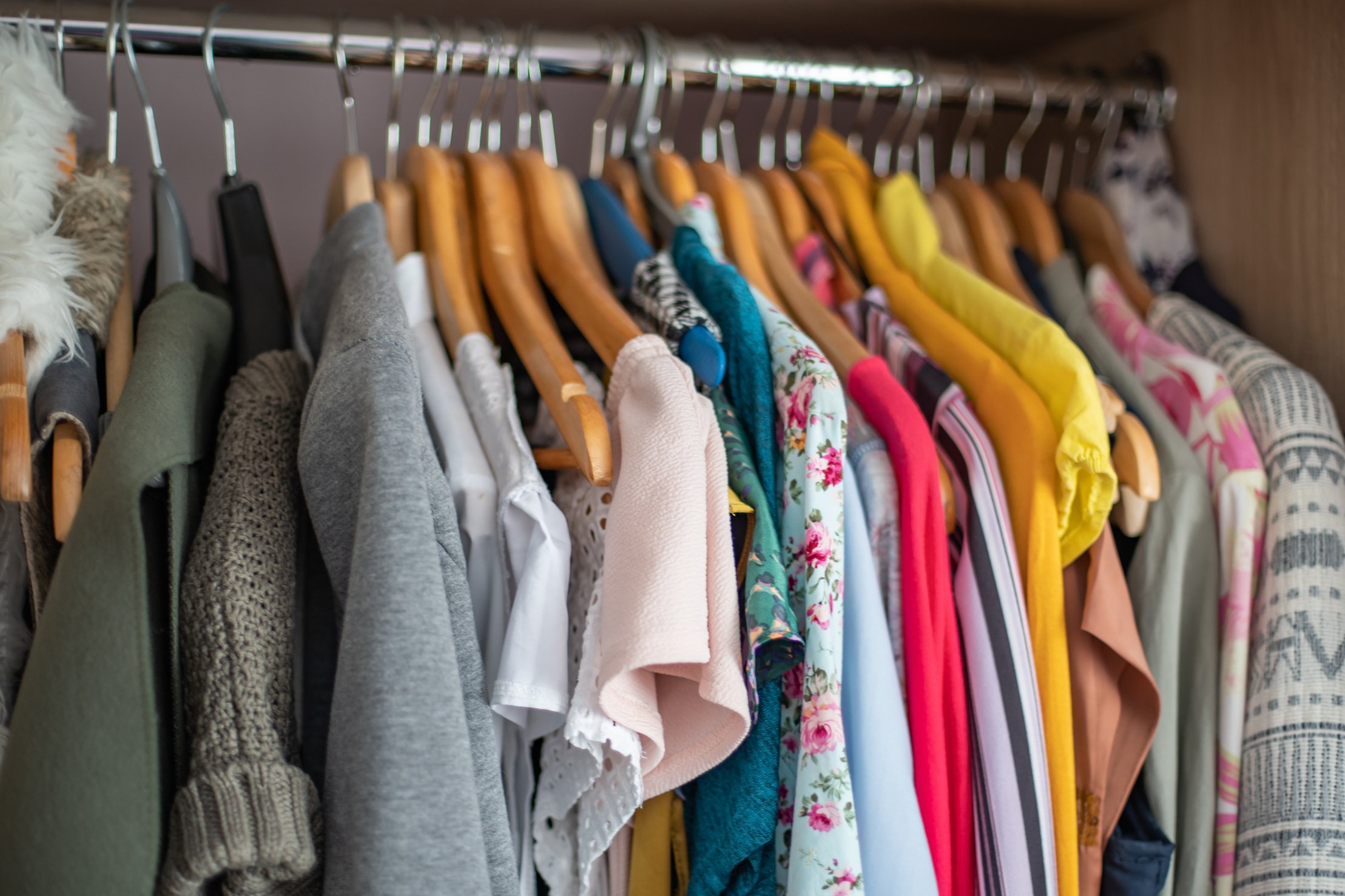 Wardrobe closet full of colorfull clothes in dressing-room.